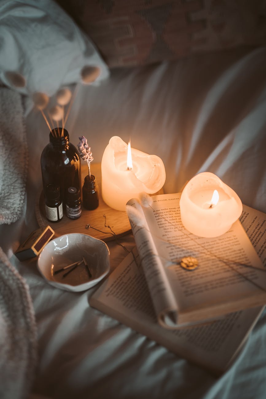 pexels-photo-4099355 lighted candle on white book beside black glass bottle